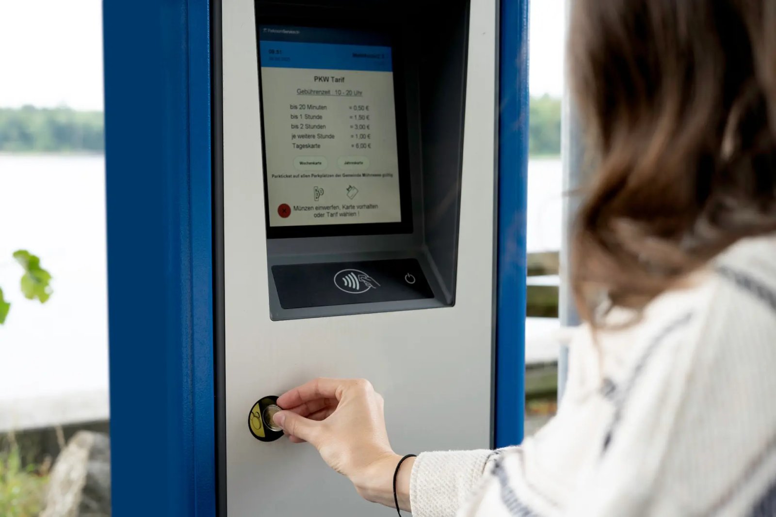 Eine Frau am Parkscheinautomaten CWT Compact S5 bezahlt die Parkgebühr mit Münzen